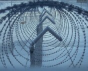 A barbed-wire fence with cameras on top at a prison.